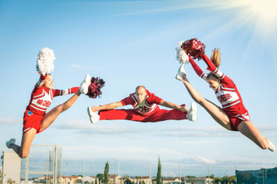 Young girls teenager cheerleaders team performing a jump with male coach