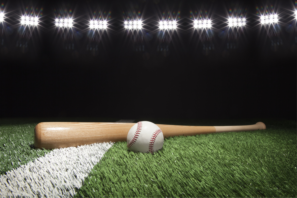 Baseball and bat at night under stadium lights on grass field with white stripe