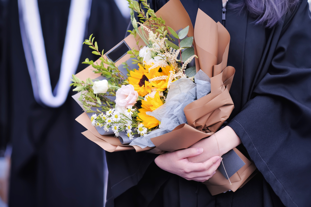 Graduates in academic dresses holding beautiful gorgeous bouquet