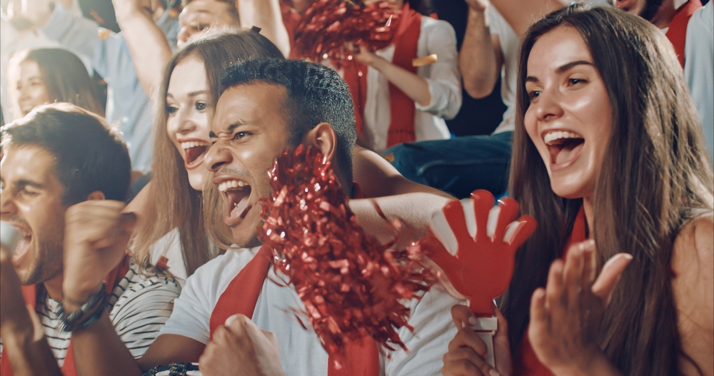 Group of fans cheer for their team victory on a stadium bleachers.