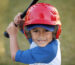 boy with red baseball helmet over a blue hat and blue tee shirt.