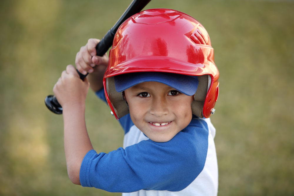 boy with red baseball helmet over a blue hat and blue tee shirt.